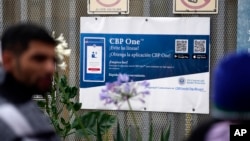 ຜູ້ຄົນ ພາກັນຢືນລໍຖ້າເພື່ອຂໍລີ້ໄພ ຢູ່ຕໍ່ໜ້າປ້າຍຂອງແອັບໂທລະສັບ CBP One, ໃນຂະນະທີ່ພວກເຂົາ ໄດ້ຕັ້ງສູນຂອງພວກເຂົາເຈົ້າຢູ່ໃກ້ທາງເຂົ້າບໍລິເວນຄົນຍ່າງ ຂອງທາງເຂົ້າທ່າເຮືອ ຊານ ອິຊິໂດຣ (San Isidro Port), ເຊິ່ງເຊື່ອມຕໍ່ເມືອງທີຮວນນາ (Tijuana) ຂອງເມັກຊິໂກ ກັບແຊນດີເອໂກ, ວັນທີ 1 ມິຖຸນາ 2023.