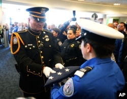 一名洛杉矶机场警员把“国家荣耀旗帜”交给交通安全局仪仗队员，纪念被枪杀的安检员贺南德兹。