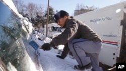在首都华盛顿近郊马里兰州的贝塞斯达，美国邮政局邮递员丹尼•金爬上他的邮递车的前盖刮扫盖住车窗的冰雪。（2014年1月3日）