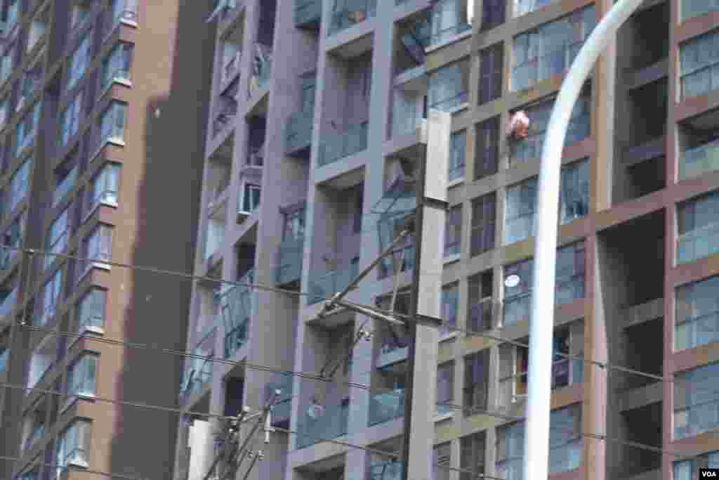 天津爆炸事故现场，核心爆炸区周围多座居民楼窗户被震碎，高速公路桥梁受损，多辆大货车被炸翻，小汽车起火或被砸，多名当地居民仍逗留在事故现场。（美国之音记者东方拍摄）