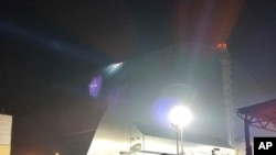 На этом снимке, опубликованном Службой Украины по чрезвычайным ситуациям, прожектор освещает повреждение, насенное ударом российского беспилотника крыше саркофага, который накрывает реактор №4 Чернобыльской АЭС. 14 февраля 2025 г. 