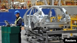 在中国重庆市福特汽车制造厂的装配线上，一名员工在汽车旁使用笔记本电脑。