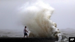 A wave crashes as a man stands on a jetty near Orleans Harbor in Lake Pontchartrain in New Orleans, June 7, 2020, as tropical storm Cristobal approaches the Louisiana coast.