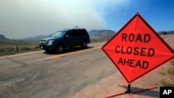 一辆汽车行驶在科罗拉多州利弗莫尔附近的拉里默郡74号公路西上。路上有“前方路段关闭”标示。背后可见野火引起的浓烟。（资料照）