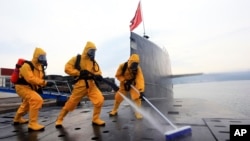 中國海軍發布的照片​​顯示，在青島潛艇基地，穿著防護服的水兵清潔核潛艇 