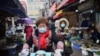 一名戴着口罩的妇女骑着电动车穿过武汉市的一个市场。（2020年1月24日）