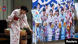 身著夏季和服的日本女性在東京一家彈珠機遊戲廳前灑水，儀式通過向地表潑水，用水蒸發吸熱達到降溫目的。