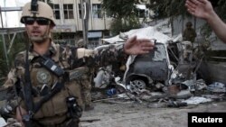 阿富汗安全部队的成员在一辆被炸弹爆炸所损坏的外国车前进行巡查（2015年8月22日）。