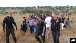 FILE - Ukrainian police officers escort the Roma residents from the village of Loshchynivka, Odessa region, Ukraine, in this image made from video taken Aug. 28, 2016. Ukrainian police evacuated a group of Roma residents from a southern town after villagers ransacked their homes.