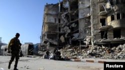 效忠敘利亞總統阿薩德的部隊一名成員拿著武器走過政府軍控制的阿勒頗城區的一座樓房廢墟。 （2016年12月9日）