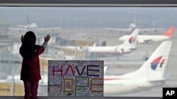 在馬來西亞吉隆坡國際機場，一名女孩透過窗戶眺望停機坪，身旁是公眾寫的“保持希望”的標語牌。