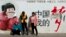 Passengers wait in front of a broken propaganda poster featuring "the China Dream" outside the Kunming Railway Station in Kunming, in western China's Yunnan province, Sunday, March 2, 2014.