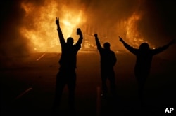 In this Nov. 25, 2014 file photo, people watch as stores burn in Ferguson, Mo.