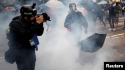 一名頭戴標有“媒體”字樣頭盔，前胸掛記者證的攝影記者在催淚彈的煙霧中拍攝香港的反送中抗議。（2019年10月6日） 