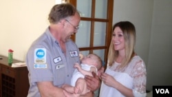 Mechanic and volunteer EMT Jeff Olson visits the baby whose life he saved last September. Mother Karen Garrison looks on in Spokane, Washington. (VOA/T. Banse)