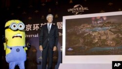 环球主题乐园及度假村集团主席、首席执行官汤姆•威廉姆斯在北京公布了主题公园的未来展示图后，和卡通电影人物小黄人(Minion)站在一起。（2014年10月13日）