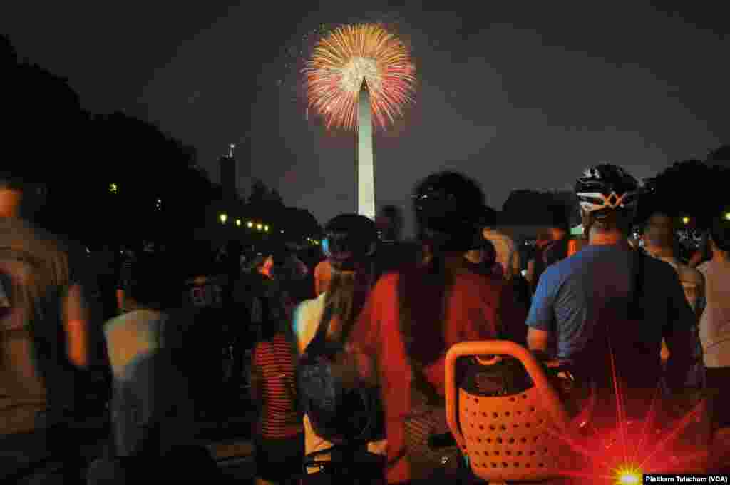 美国人在首都华盛顿的国家大草坪上观赏焰火，礼花在华盛顿纪念碑上空绽放（2017年7月4日）。