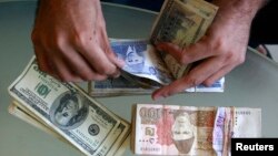 A currency dealer counts Pakistani rupees and U.S. dollars at his shop in Karachi October 8, 2008. The Pakistani rupee sank to a record low of 80.30 to the dollar on Wednesday due to unrelenting pressure from import payments and an erosion of confidence i