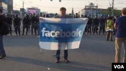 社交网站已成为俄罗斯和乌克兰民众串联上街抗议的主要工具。在去年普京就职总统前夕的5月6日莫斯科大规模反政府抗议中，一名示威者在防爆警察前手持脸书旗帜。(美国之音 白桦拍摄)