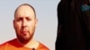An image grab taken from a video released by the Islamic State (IS) and identified by private terrorism monitor SITE Intelligence Group purportedly shows U.S. freelance writer Steven Sotloff dressed in orange and on his knees in a desert landscape speaking to the camera before being beheaded by a masked militant (R), Sept. 2, 2014. 