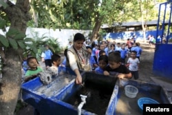 Health promoter Marielos Sosa deposits fishes in a water tank at a local school for a mosquito control project at San Diego village in La Libertad, El Salvador, Feb. 1, 2016.