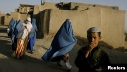 An Afghan boy watches as a group of women walk by in the old city of Ghazni, August 19, 2007. (Click to Expand)