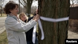 Carla Sloan (L) and Liz Ziehl, friends and neighbors of diplomat Anne Smedinghoff, who was killed in Afghanistan, tie a ribbon on a tree in River Forest, Illinois, April 8, 2013. 
