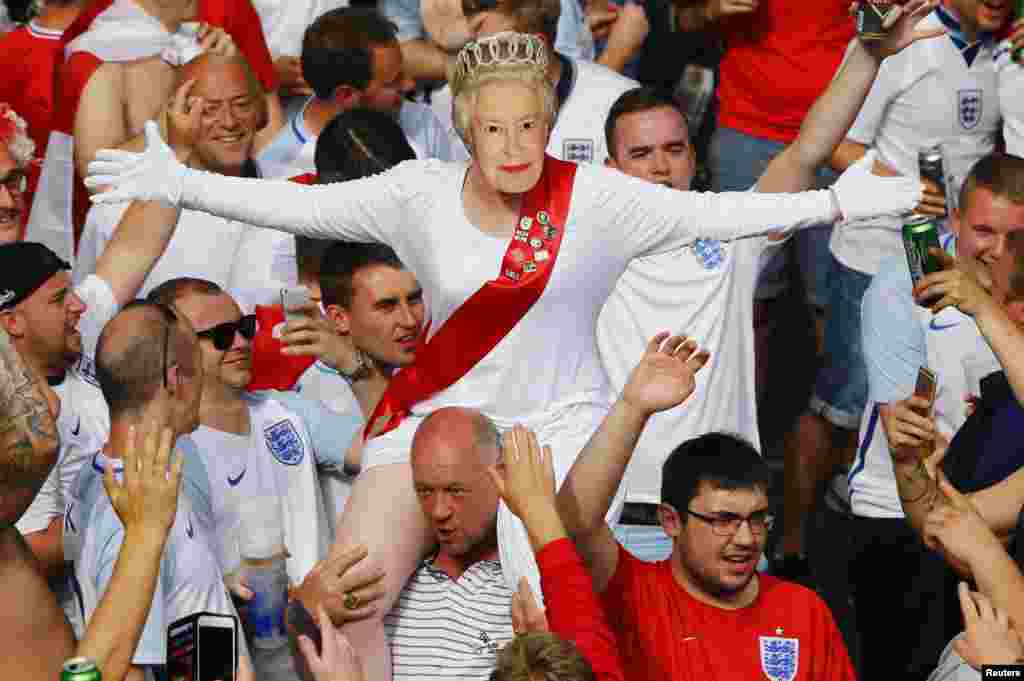 2016年6月20日，在英国足球队同外国球队比赛前，一位英国球迷带着女王的面具，坐在同伴的肩上