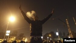 一名反穆尔西抗议者2012年12月6日在一批阻挡人们前往开罗总统府通道的共和卫队的前面抽烟和摆手势