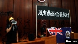 一名进入香港立法会的抗议者站在挂在立法会内的港英旗帜旁使用扩音喇叭讲话。（2019年7月1日）