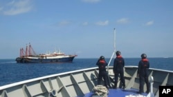 ໃນ​ຮູບ​ວັນ​ທີ 27 ເມ​ສາ 2021 ທີ່​ຖືກ​ສະ​ໜອງ​ໃຫ້​ອົງ​ການ​ຍາມ​ຊາຍ​ຝັ່ງ ຟີ​ລິບ​ປິນ, ສະ​ແດງ​ໃຫ້​ເຫັນ​ເຈົ້າ​ໜ້າ​ທີ່​ລາດ​ຕະ​ເວນ​ຢູ່​ຂ້າງ​ກຳ​ປັ່ນ​ທີ່​ຖືກ​ກ່າວ​ວ່າ​ເປັນ​ກຳ​ປັ່ນ​ທະ​ຫານ​ບ້ານ ຈີນ ຢູ່​ໝູ່​ເກາະ ຊາ​ບີ​ນາ ໃນ​ທະ​ເລ​ຈີນ​ໃຕ້.