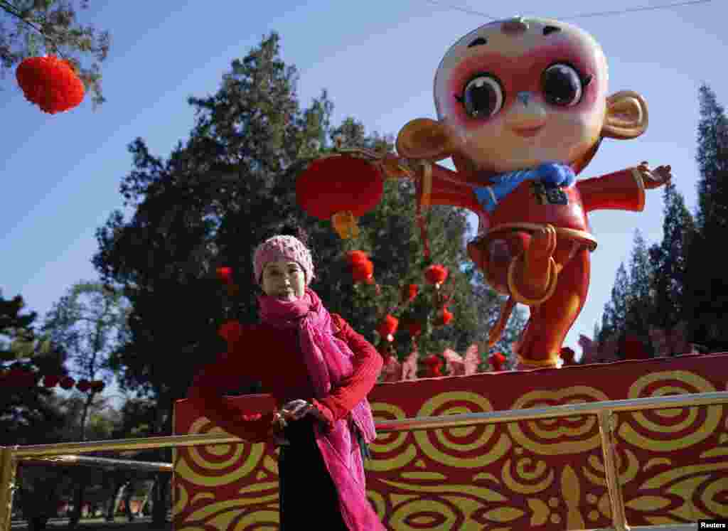 在春节前夕，在北京地坛庙会，一位妇女在猴子造型前面摆姿势照相（2016年2月5日）