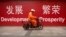 FILE - A maintenance worker rides a scooter past banners reading "Development" and "Prosperity" in English and Chinese on a street in central Beijing, July 15, 2015.