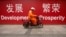 FILE - A maintenance worker rides a scooter past banners reading "Development" and "Prosperity" in English and Chinese on a street in central Beijing, July 15, 2015.