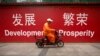FILE - A maintenance worker rides a scooter past banners reading "Development" and "Prosperity" in English and Chinese on a street in central Beijing, July 15, 2015.