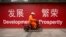 FILE - A maintenance worker rides a scooter past banners reading "Development" and "Prosperity" in English and Chinese on a street in central Beijing, July 15, 2015.