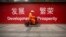 FILE - A maintenance worker rides a scooter past banners reading "Development" and "Prosperity" in English and Chinese on a street in central Beijing, July 15, 2015.