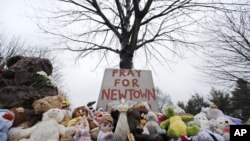 Stuffed animals and a sign calling for prayer rest at the base of a tree near the Newtown Village Cemetery in Newtown, Conn., Dec. 17, 2012. 