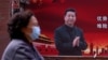 一位戴口罩的妇女从习近平的宣传画前走过（2020年3月12号）。