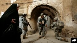 一名伊拉克婦女走過在摩蘇爾地區一個警察局站崗的美軍士兵。（資料照片）